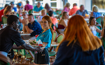 Waitress smiling serving food with people in the backdrop