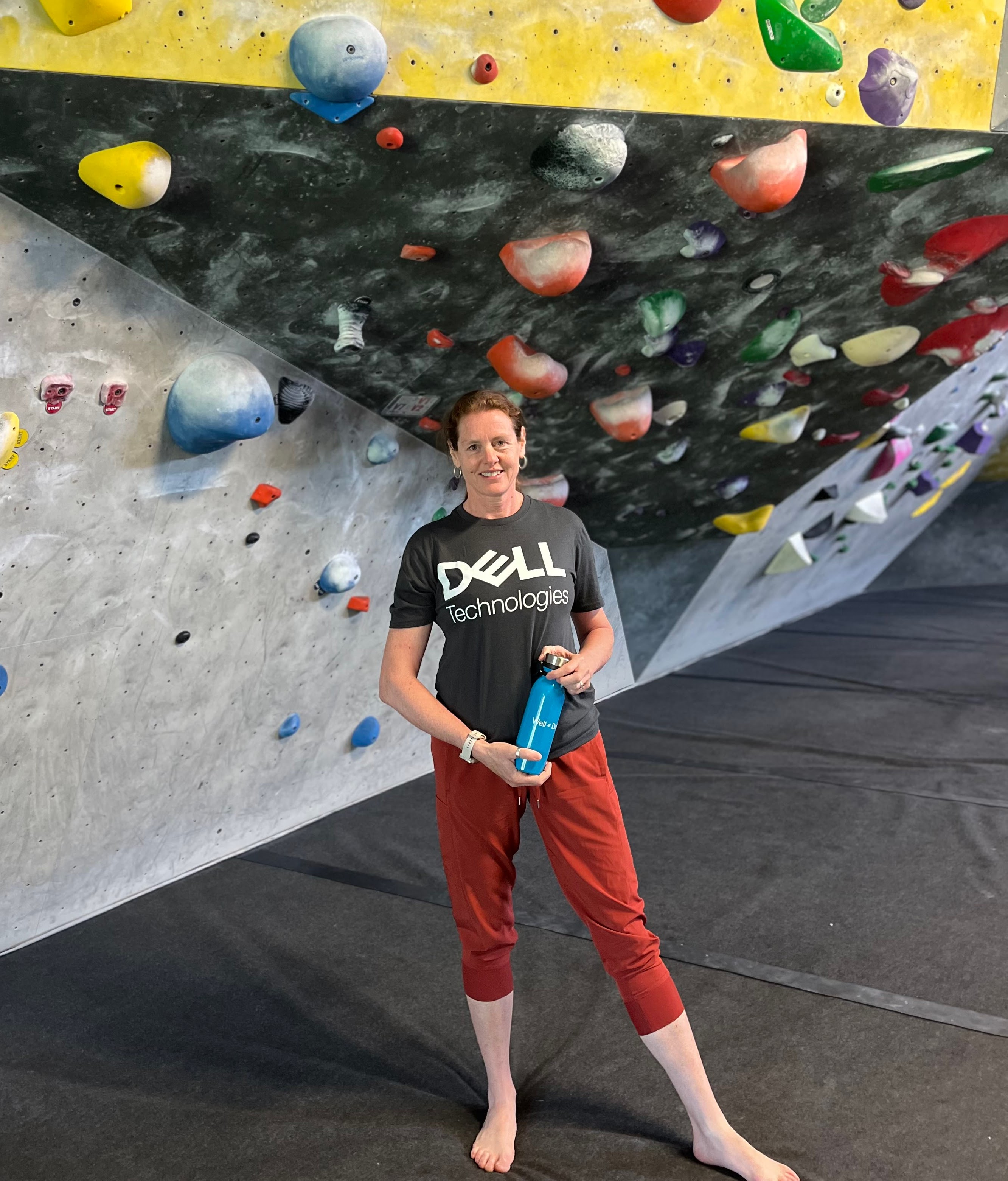 Michelle poses in front of a rock climbing wall.