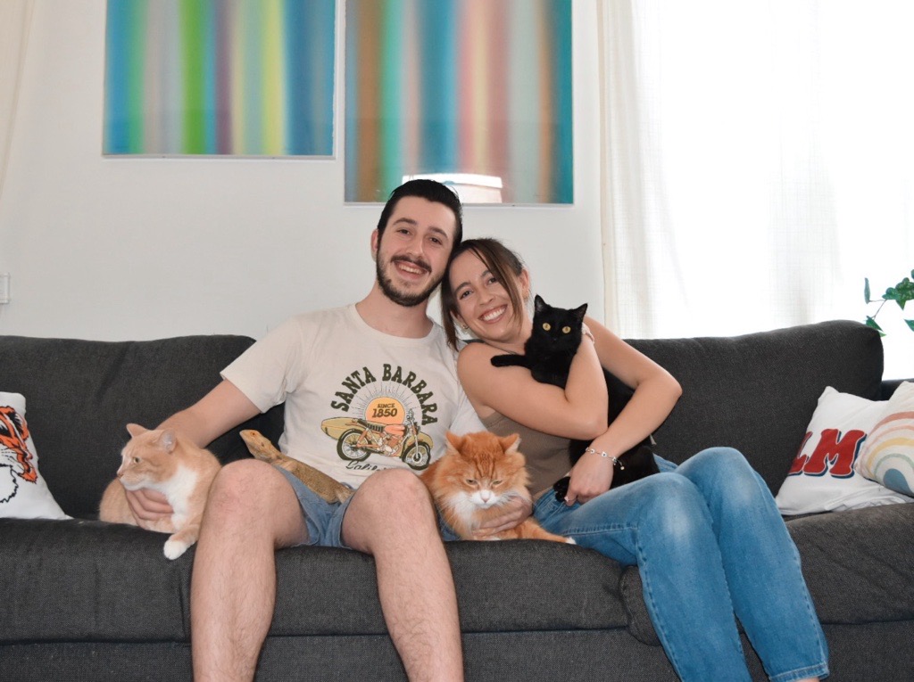 Athena sits on a couch with a man and three cats.