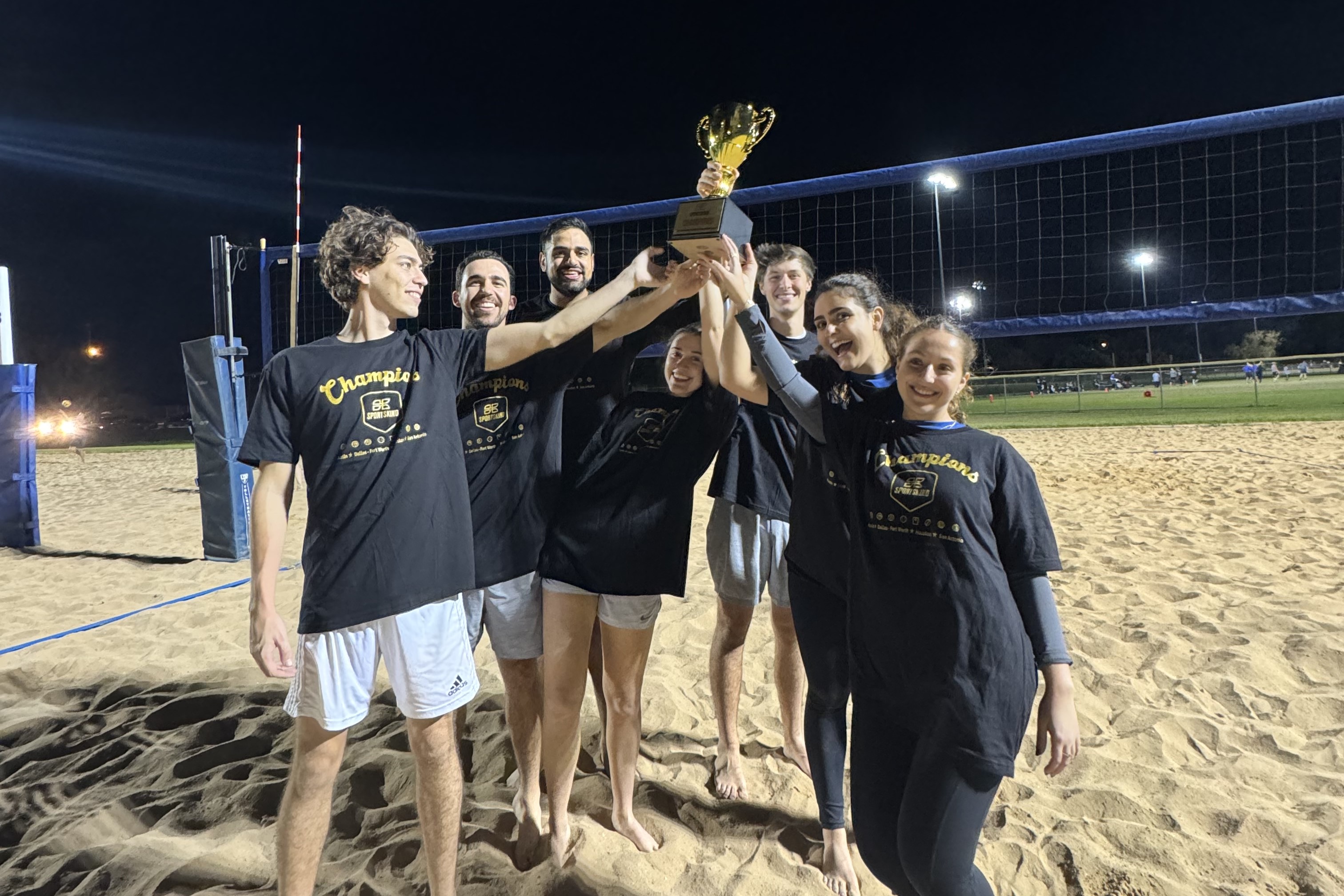 A group of SCDP volleyball players hold a trophy high while celebrating.