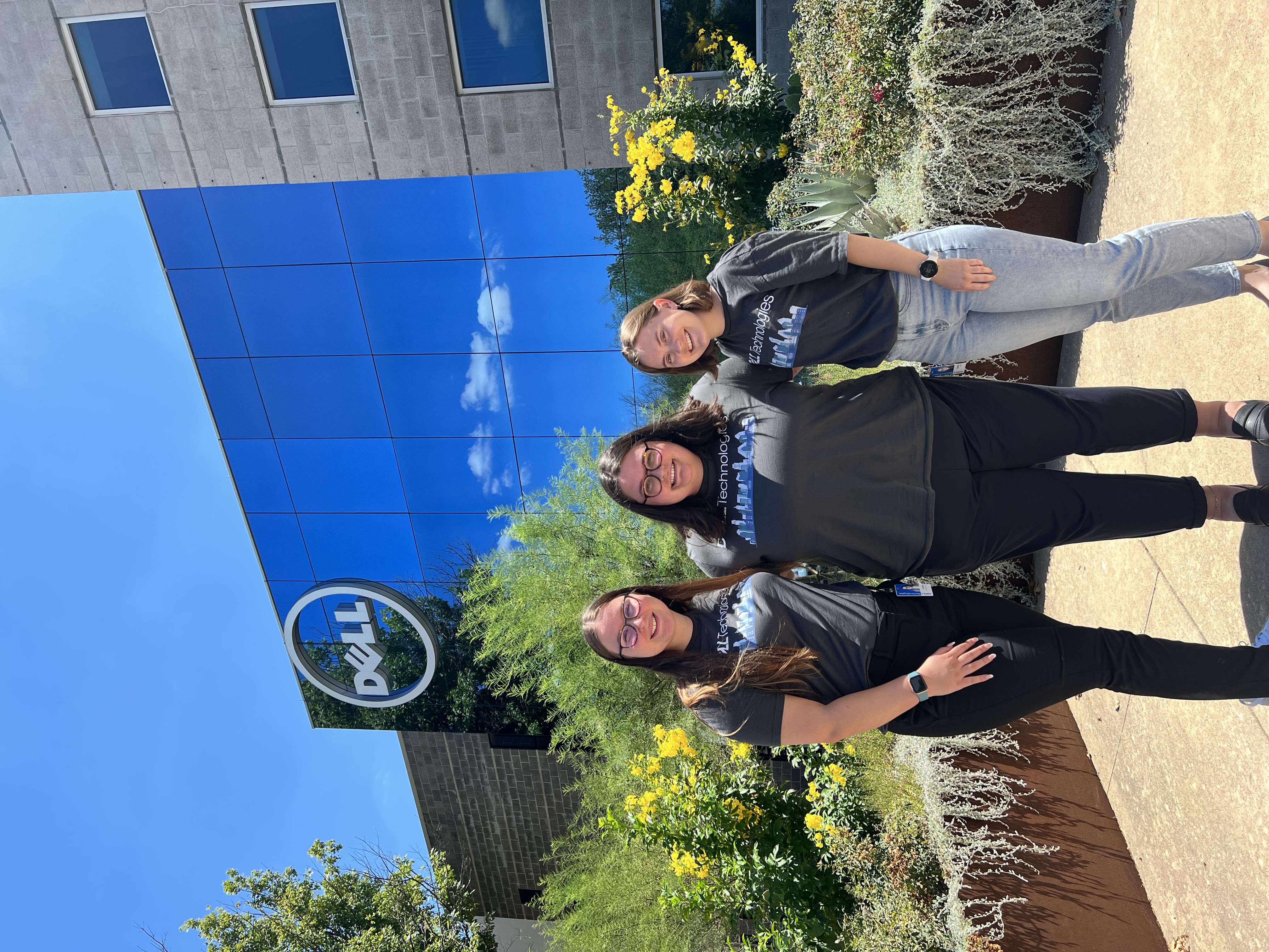 Nova and two other women stand outside a Dell Technologies building in matching Dell Technologies t-shirts.