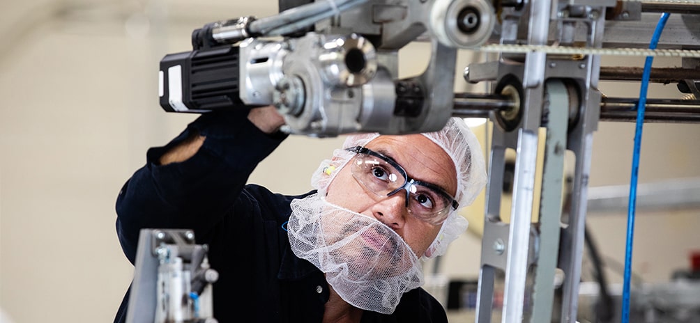 Man wearing protective goggles, hair net and mask while operating a machine