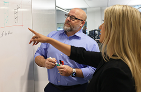 Two professionals collaborating in front of a whiteboard.