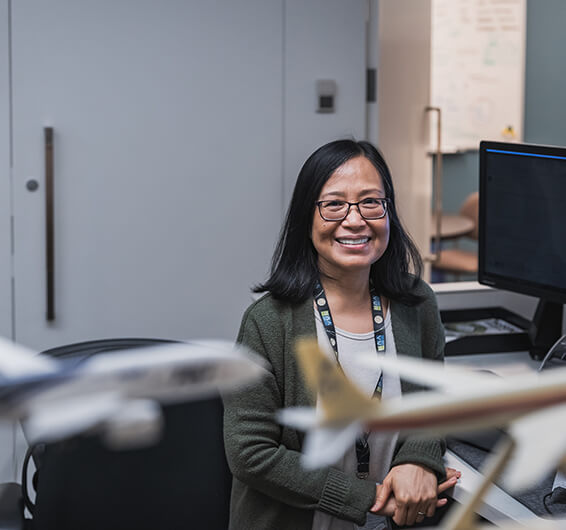 Une employée sourit assise à un bureau, avec des maquettes d'avions au premier plan