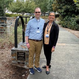 Bradley Carson stands with a colleague in front of the Bell of Hope outside of the Duke Cancer Center