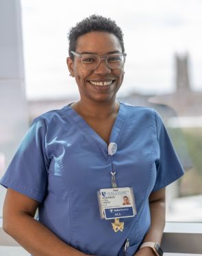 Female team member smiles in blue scrubs with the Duke chapel in the distance.