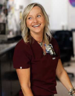 Female team member in maroon scrubs smiles.