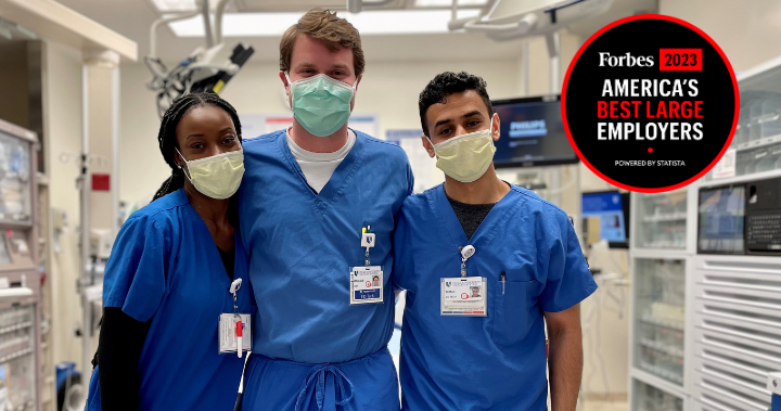 Three team members in blue scrubs smile together.