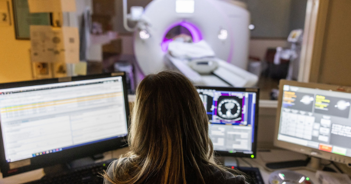 Female team member looking at screens with CT scanner in the background.