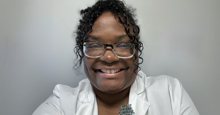 Shanel smiles in glasses and a white lab coat.