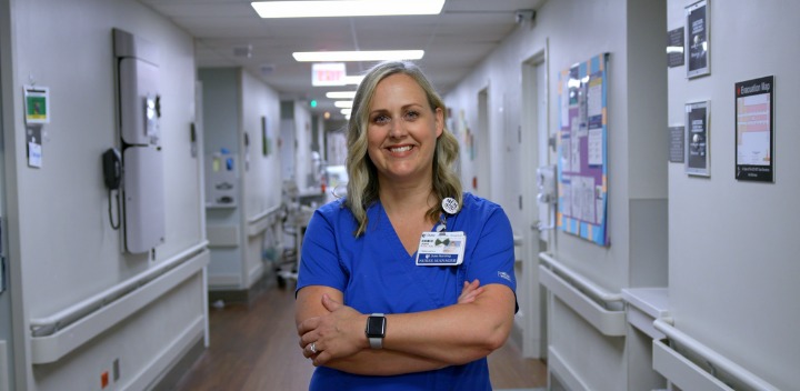 nurse joni folding arms smiling in blue scrubs in the hospital hallway.