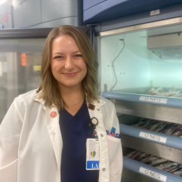 Meghan smiles in lab coat in front of equipment.