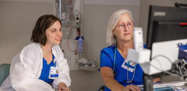 two nurses discuss patient care at a computer.