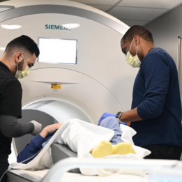 george helps a patient into an MR machine with a colleague.