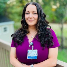 Jessica smiles in maroon scrubs outside.