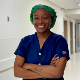 Kee smiles in a scrub hat and blue scrubs.