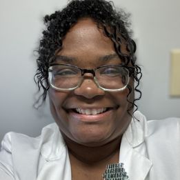 Shanel smiles in glasses and a white lab coat.