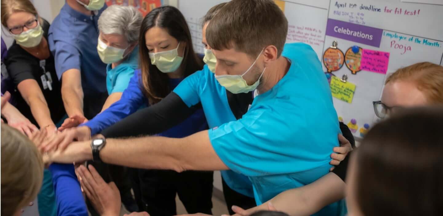 Group of employees putting hands together in middle of circle to be a team and support each other in providing great care