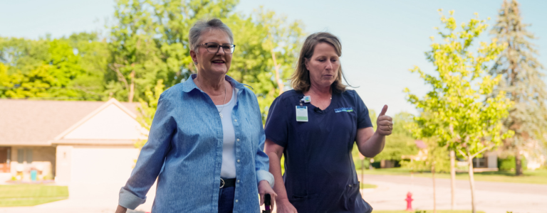 Home health nurse and patient walking outside while having a conversation.