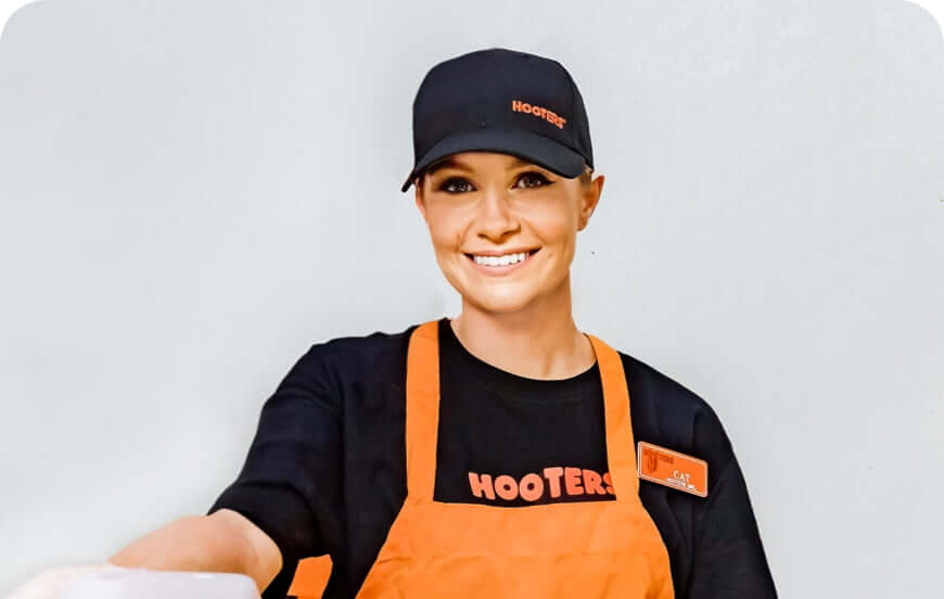 female Hooters line cook smiling and holding out a to-go meal container
