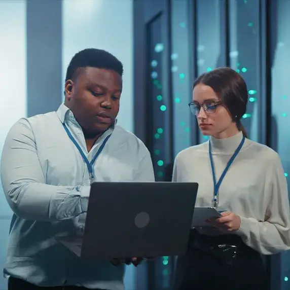 Two people looking at a laptop in front of servers