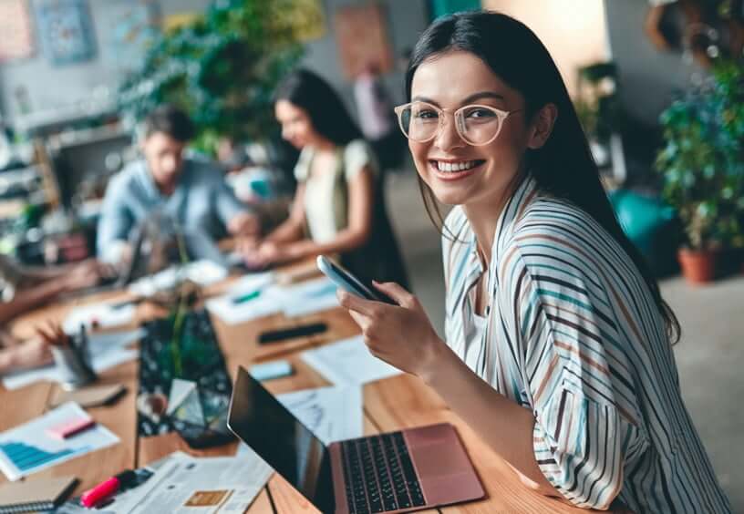 woman looking at phone by her computer