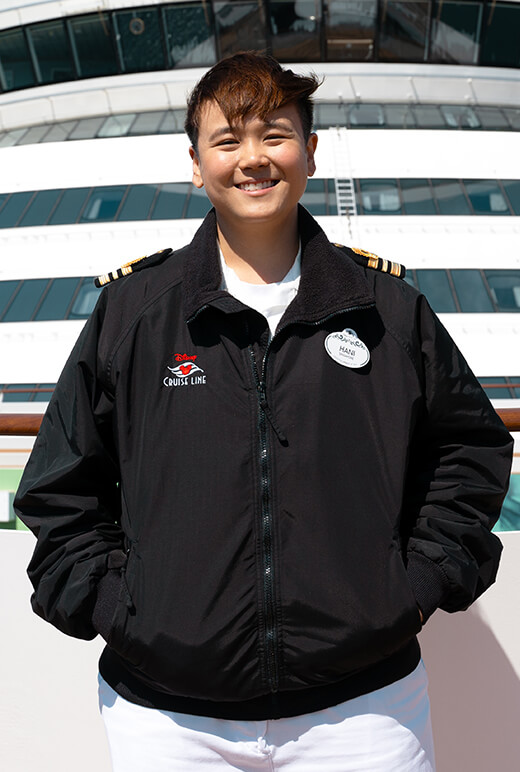 Hani at the prow of a cruise ship, wearing a uniform and smiling