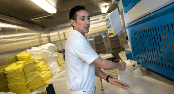 Male staff member wearing a white shirt folding white linen in the laundry room