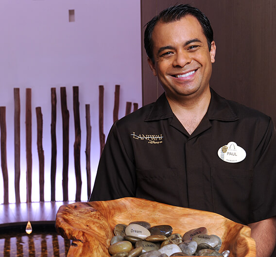 Man smiling with a wooden bowl of smooth rocks