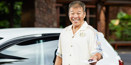 A man who appears to be a valet, smiling and handing over car keys.