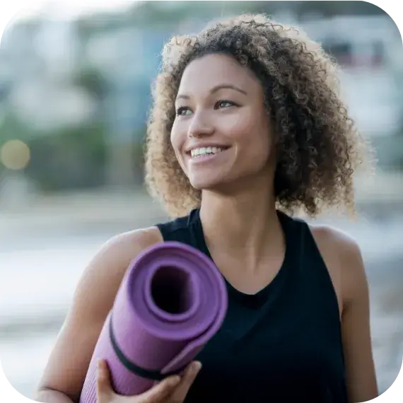 Fit woman holding a yoga mat at the beach