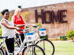 image of two people on bikes with a 'HOME' sign in background