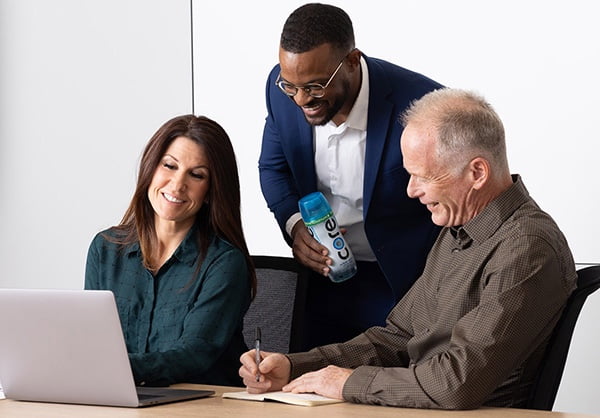 2 men and 1 woman look at a laptop. 