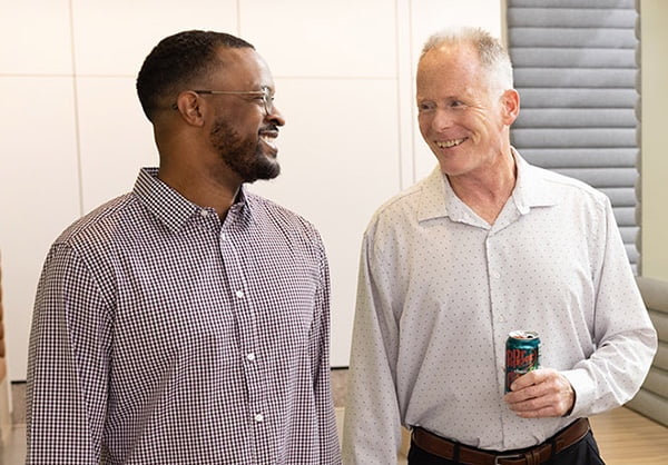 Two male employees talking, one is carrying a can of soda. 