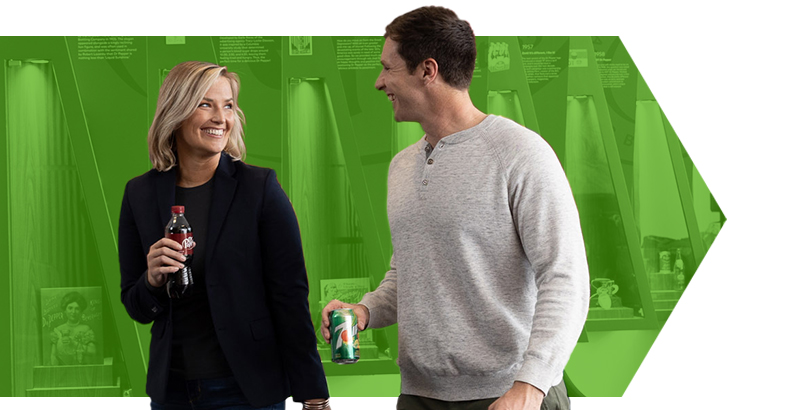 Male and female employee walking in a corporate location while holding drinks. 