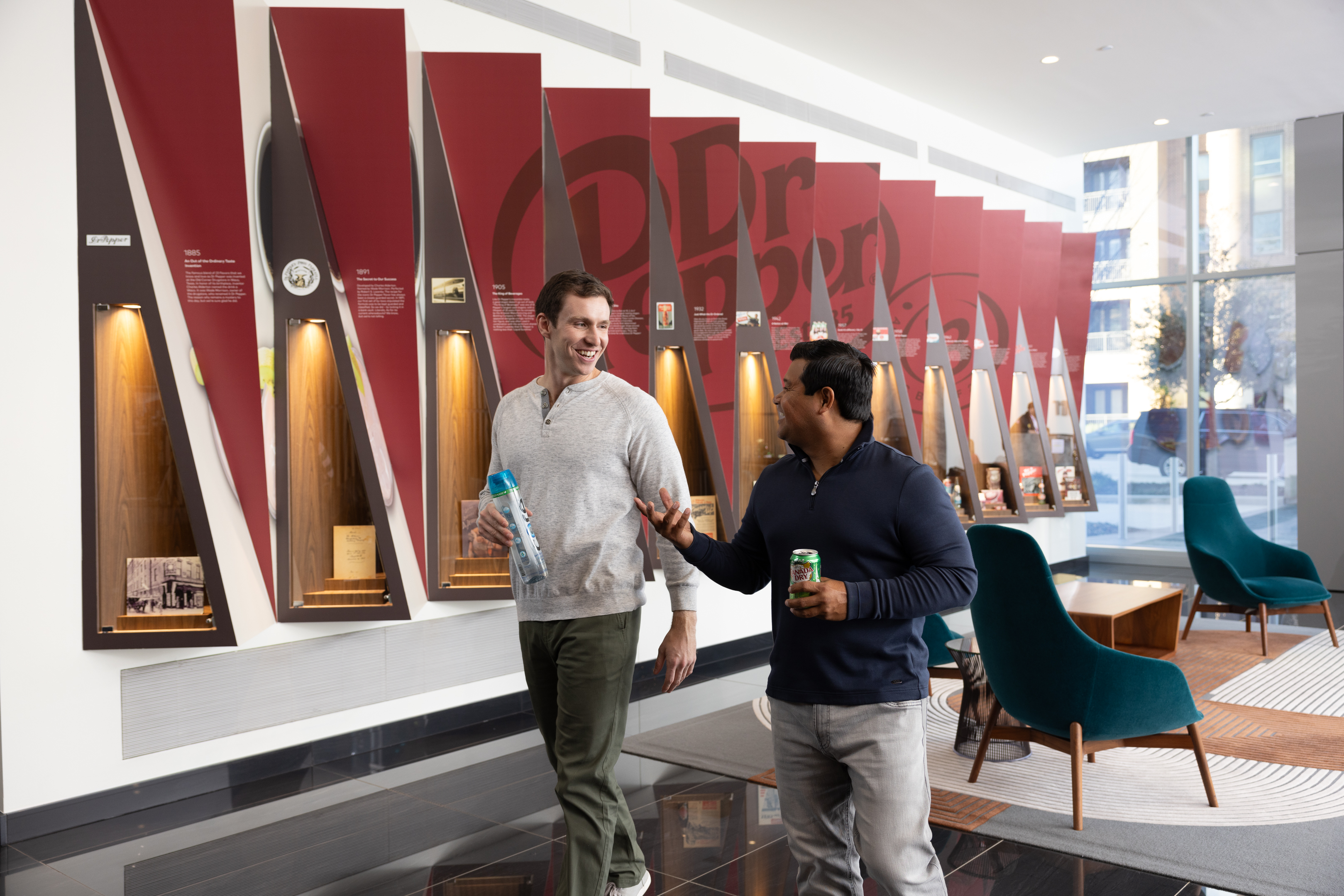 Male and female employee walking in a corporate location while holding drinks. 