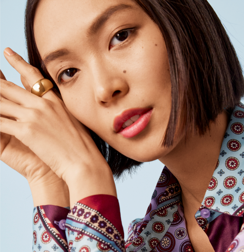 Woman in patterned silk shirt and gold earrings.