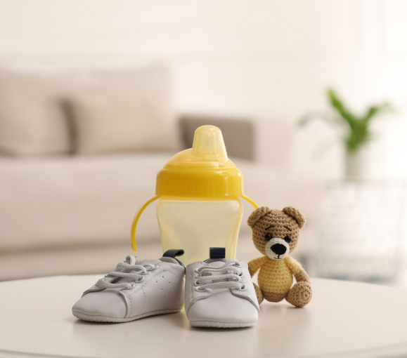 Baby shoes next to baby bottle and knitted bear toy.