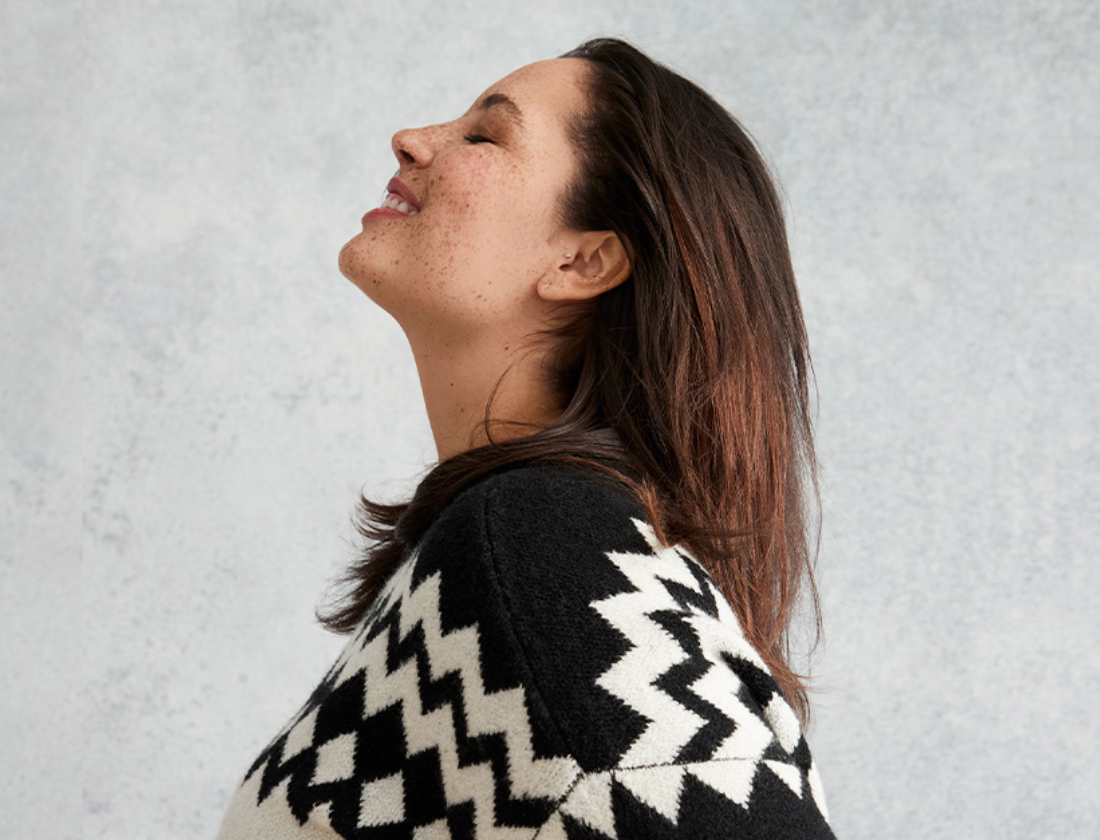 Smiling woman with head tilted back in a black and white sweater.