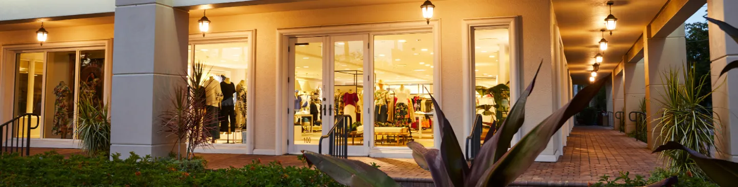 outdoor shopping storefront with large glass doors, warm hanging lanterns, and square white columns