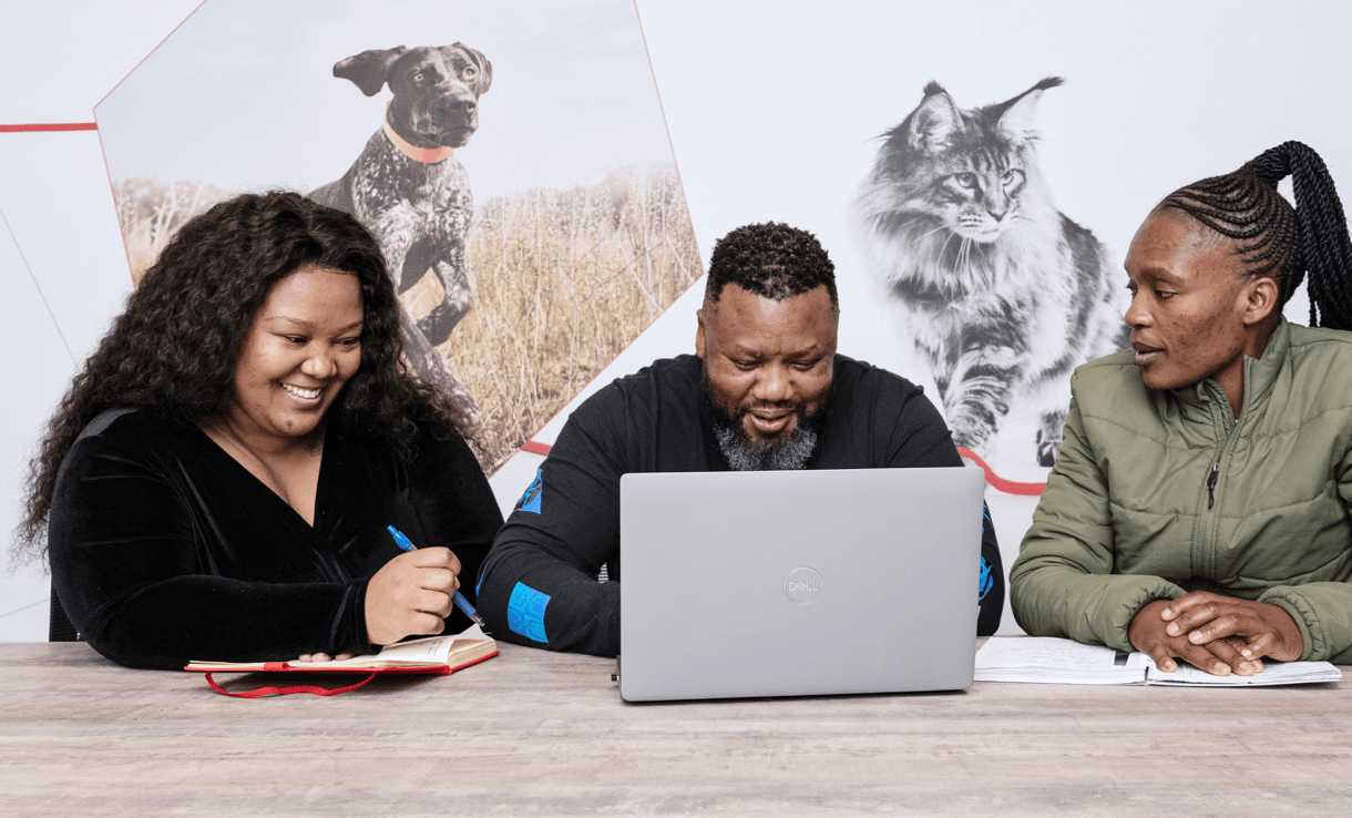 Three employees working together at a desk in front of a laptop.