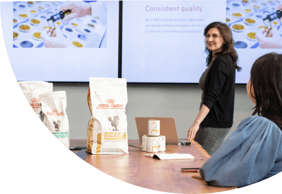 People meeting around a large office table, with Royal Canin products sitting on the table and large screens that display "Consistant quality".