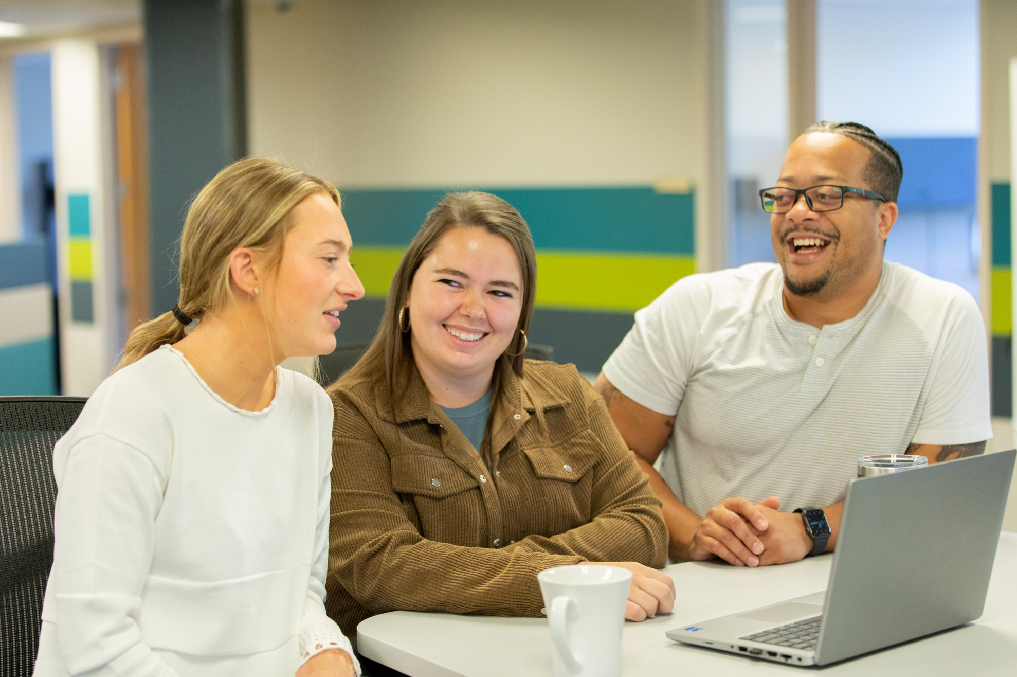 2 women and a man at a table with a laptop