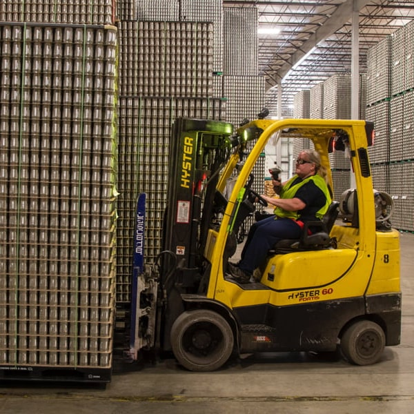 Man driving forklift truck in warehouse full of cans