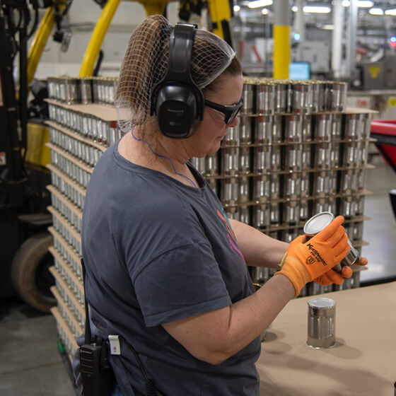 Woman inspecting a tin in uniform and wearing protective clothing for her eyes and ears