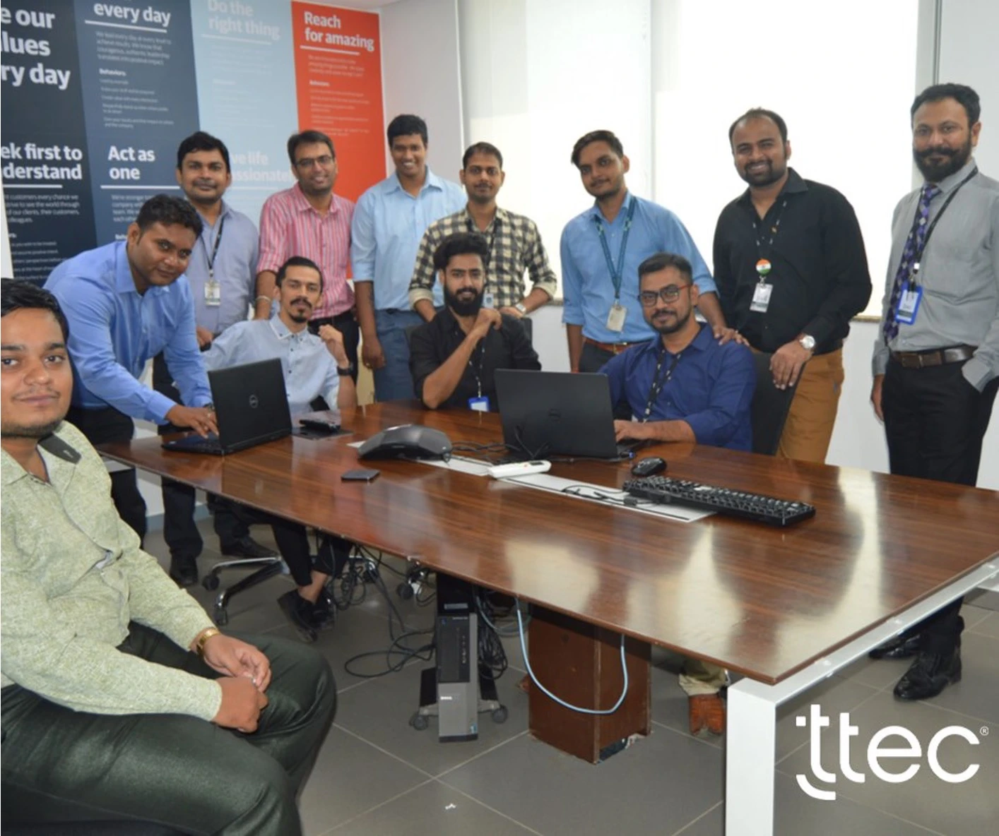 All TTEC India team members gathered around a conference table with laptops.