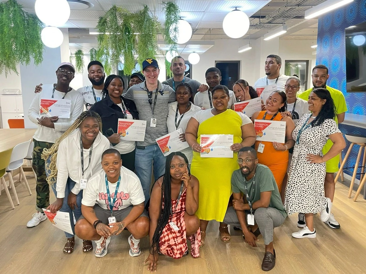 Large group of TTEC employees posing together in a modern office, holding certificates and celebrating achievements.