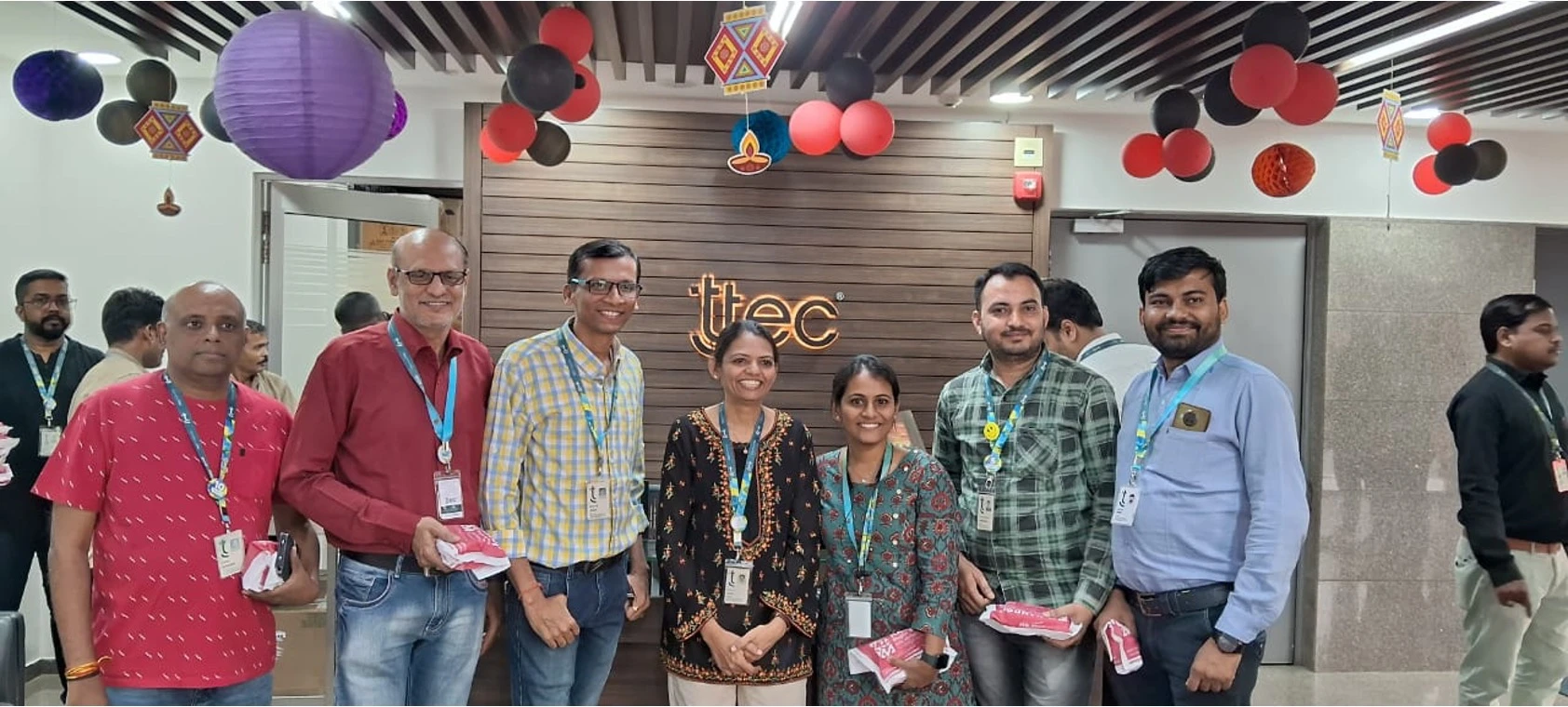 Group of TTEC employees celebrating with colorful decorations and balloons in a festive office setting.