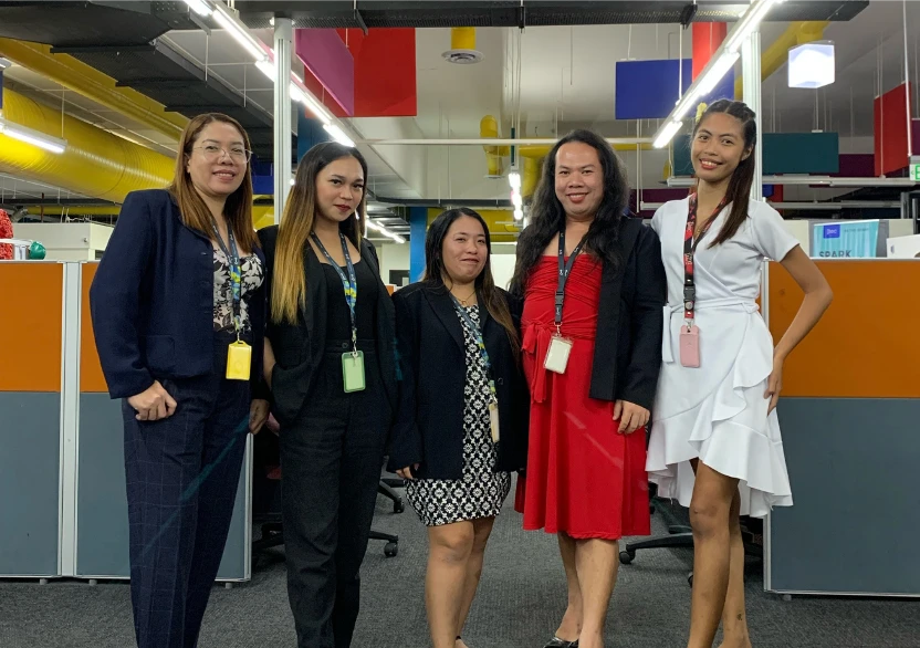 Five TTEC employees in professional attire standing together in an office workspace.