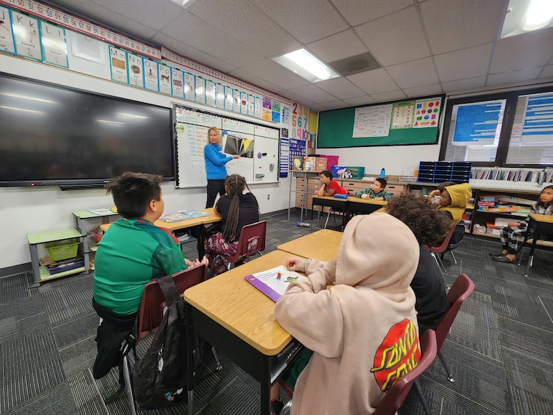 A TTEC employee and volunteer reading with kids in a classroom.
